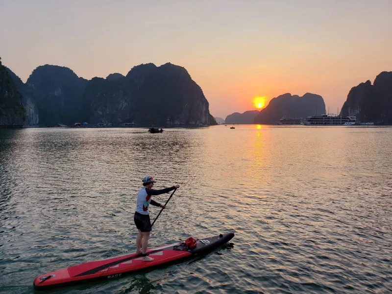 Người chèo ván đứng lướt trên mặt nước yên bình lúc hoàng hôn giữa các đảo đá vôi vịnh Hạ Long