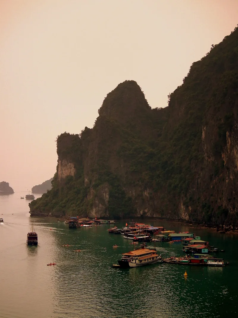 Thuyền và làng chài nổi nằm dưới chân núi đá vôi ở vịnh Hạ Long, Việt Nam.
