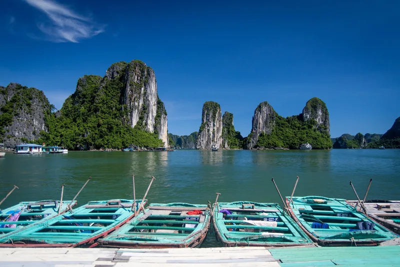 Những chiếc thuyền chèo nổi trước các đảo đá vôi sừng sững ở Vịnh Hạ Long dưới bầu trời xanh trong.