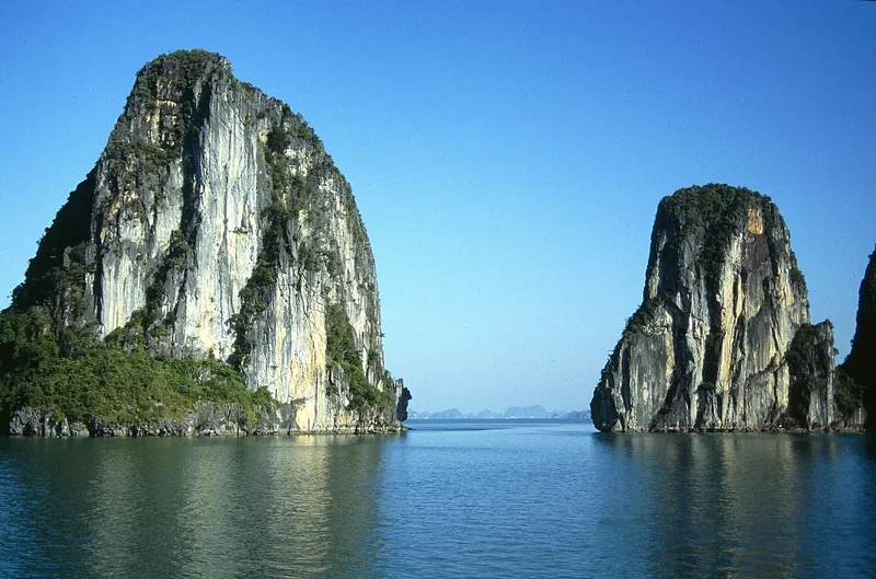 Những khối núi đá vôi sừng sững nhô lên từ mặt nước xanh lặng của vịnh Hạ Long dưới bầu trời trong xanh.