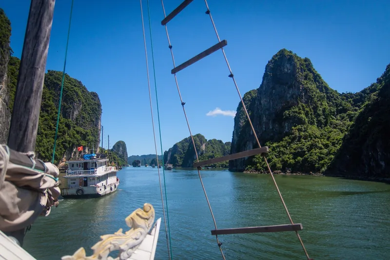 Thang dây treo trên cột thuyền, phía trước là các đảo đá vôi và tàu du lịch trên vịnh Hạ Long.