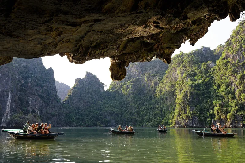 Những chiếc thuyền nhỏ chở du khách xuyên qua hang đá vôi vào khung cảnh núi đá vịnh Hạ Long, Việt Nam.