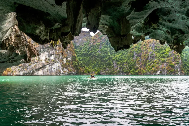 Một người chèo thuyền kayak băng qua hang đá vôi giữa những núi đá phủ cây xanh ở vịnh Hạ Long.