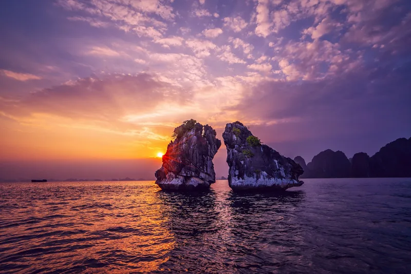 Hoàng hôn buông xuống giữa hai hòn đảo đá vôi song song trên vịnh Hạ Long, nhuộm tím cam cả mặt biển.