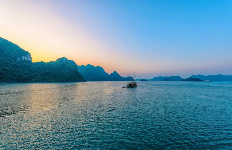 Một chiếc thuyền du lịch lững lờ giữa các đảo đá vôi khi hoàng hôn buông xuống vịnh Hạ Long.