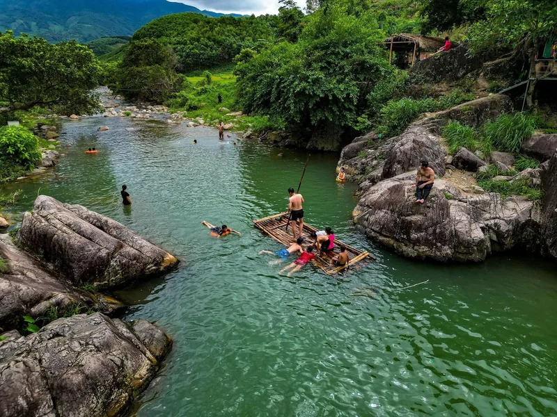 Mọi người bơi lội và chèo bè trên dòng suối xanh đá giữa đồi núi xanh tươi gần Tiên Yên.