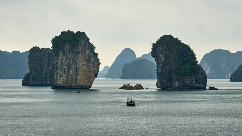 Một chiếc thuyền nhỏ đi qua giữa hai khối núi đá vôi cao sừng sững trên mặt nước yên tĩnh của vịnh Hạ Long.