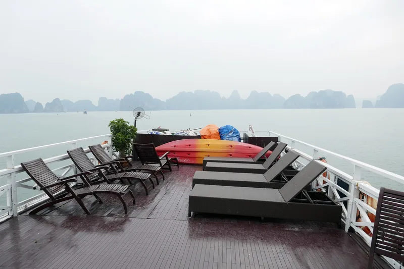 Ghế tắm nắng và xuồng kayak trên sân tàu du lịch, phía xa là các đảo đá vịnh Hạ Long